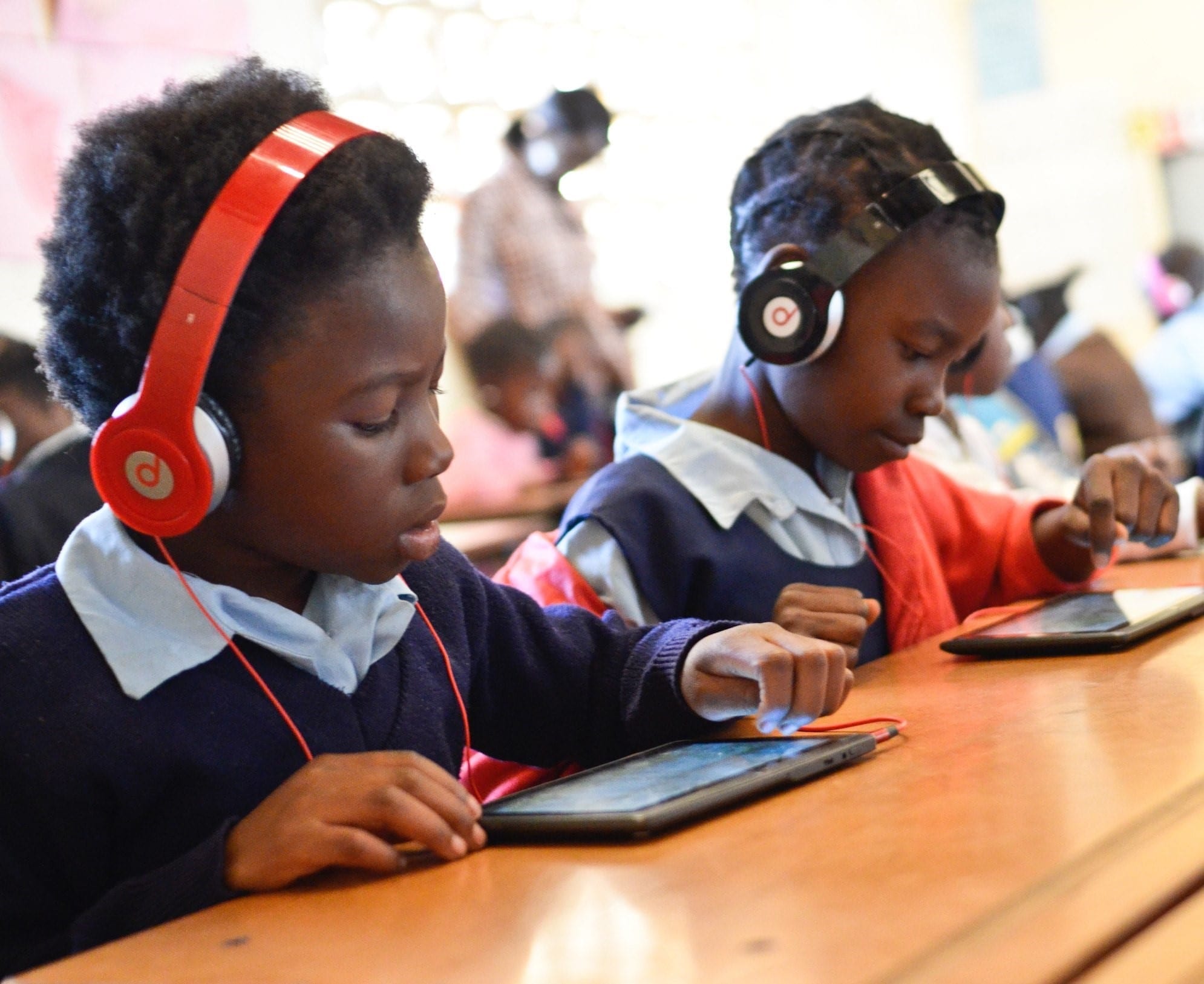 Two students use a tablet and headphones to use GraphoGame created by the Agora Center.