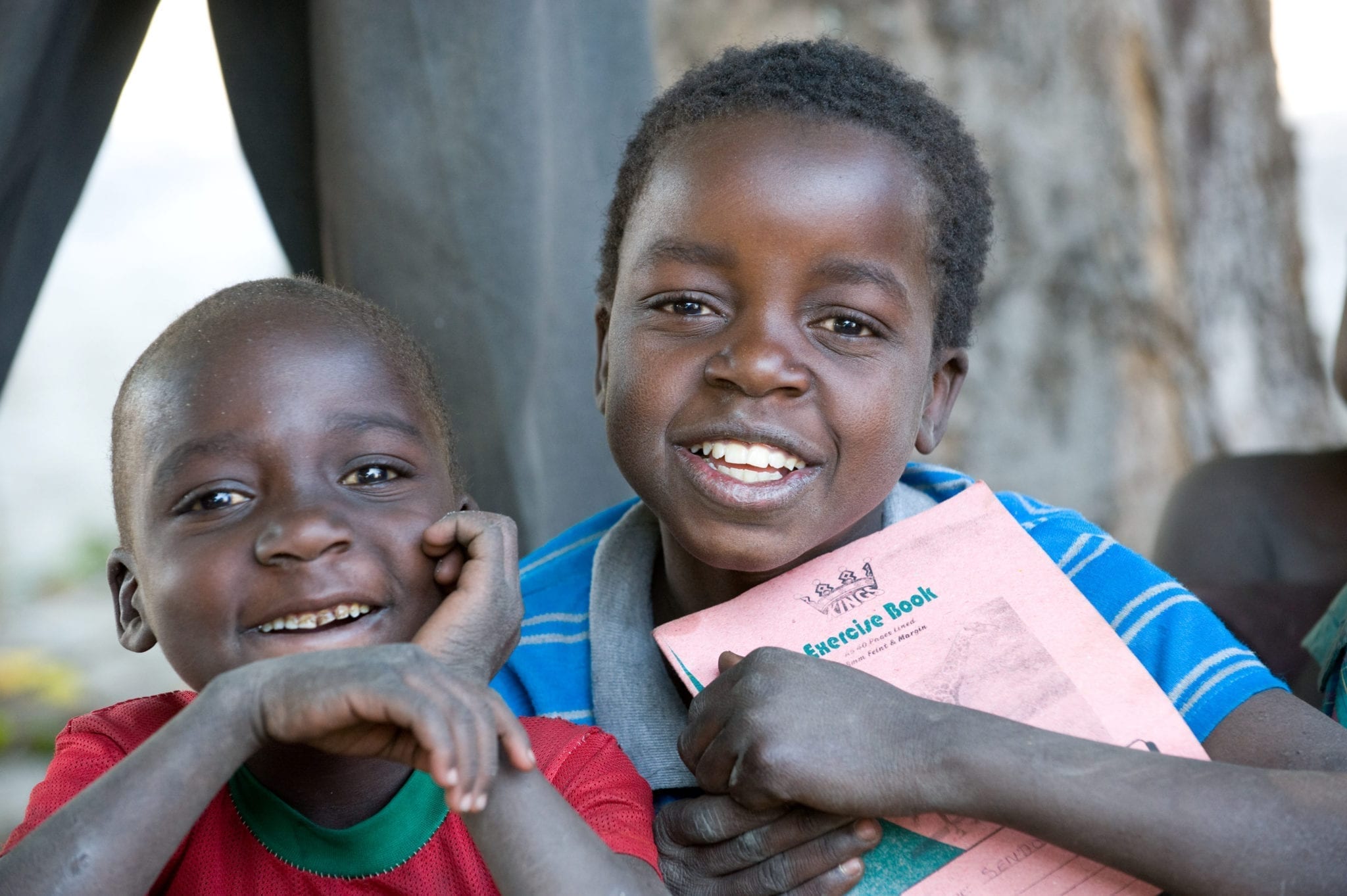Two boys in Zambia smile as they hold learning materials.