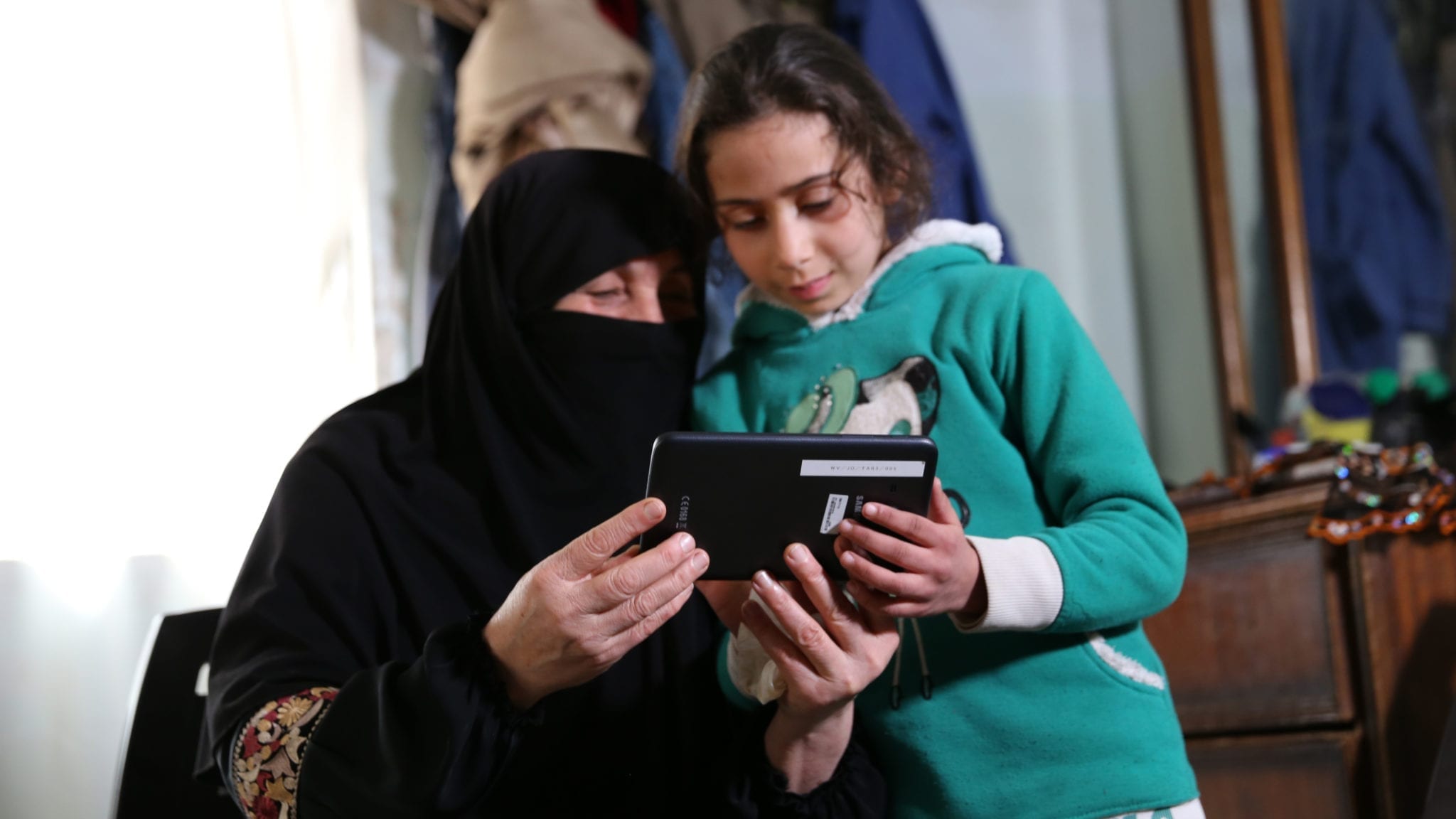 Girl in refugee camp in Jordan plays the Antura and the Letters literacy gaming app with her grandmother.
