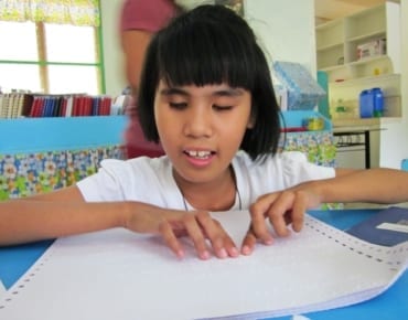 Alexa, a blind student in the Philippines, smiles as she reads a braille book provided through Resources for the Blind's "Reading Beyond Sight" project.