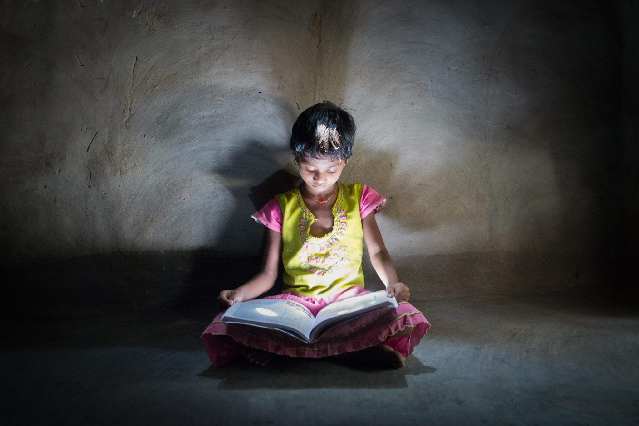 A young girl in India reads with the help of a light.