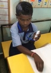 A young boy is reading a braille book while listening to the audio recording.