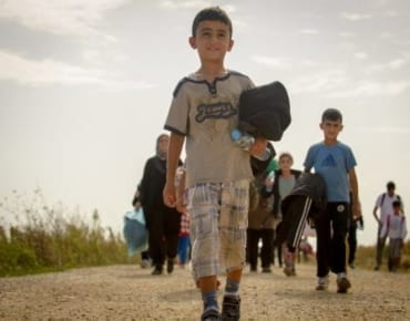 Child refugees and migrants walking while carrying their belongings.