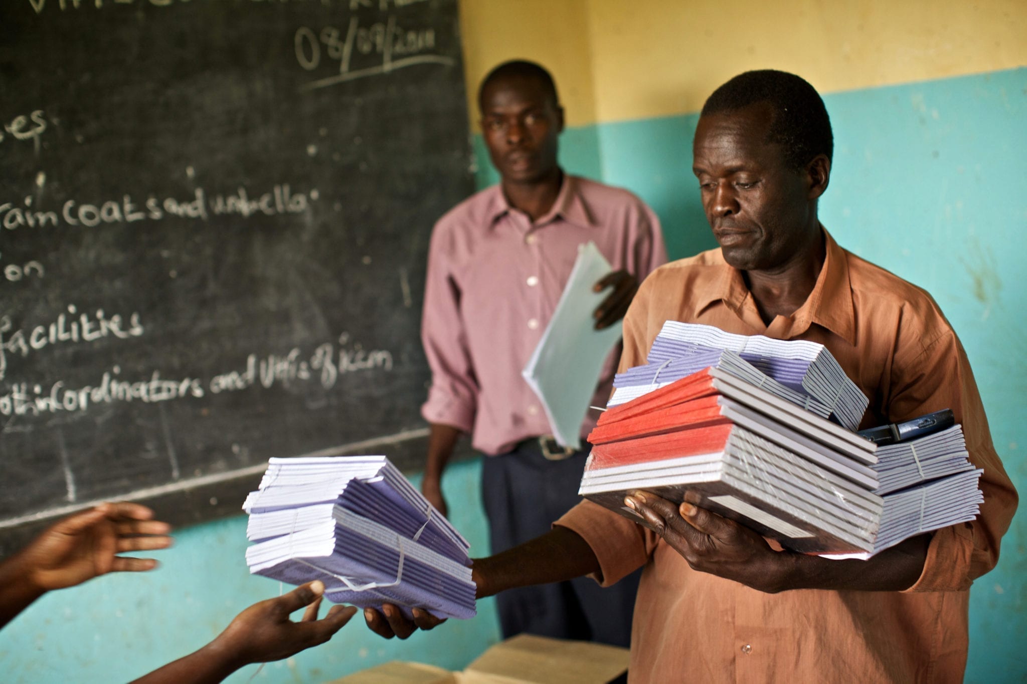 Two men distribute scholastic materials in Uganda.