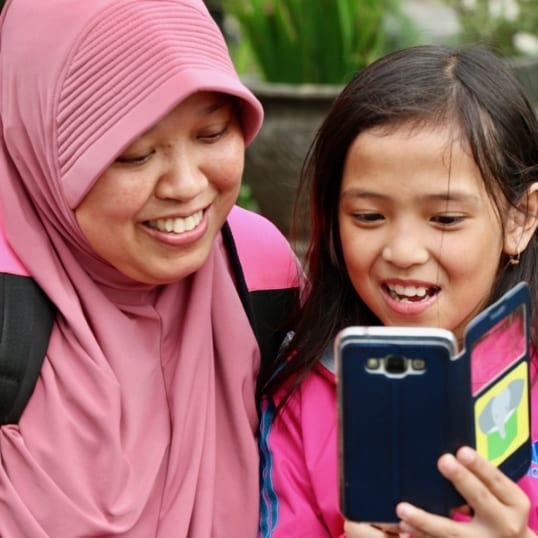 A mother and daughter enjoy stories on a mobile phone provided by ACR GCD-funded The Asia Foundation.