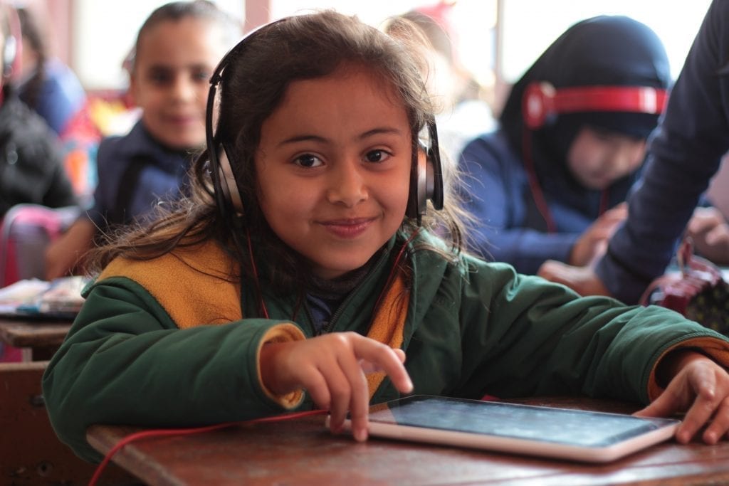 A girl wearing headphones hold a tablet featuring a collection of digital stories developed by ACR GCD-funded Little Thinking Minds in Jordan.