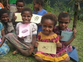 group of children sitting on grass holding books.
