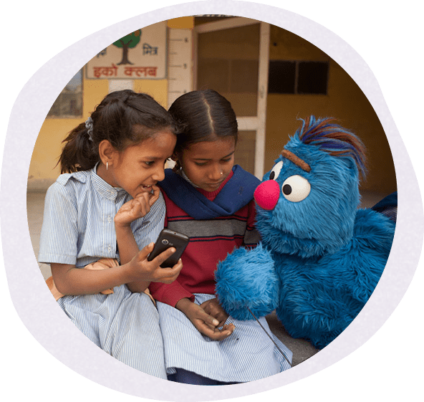 Two little girls sitting next to the cookie monster while holding a cell phone