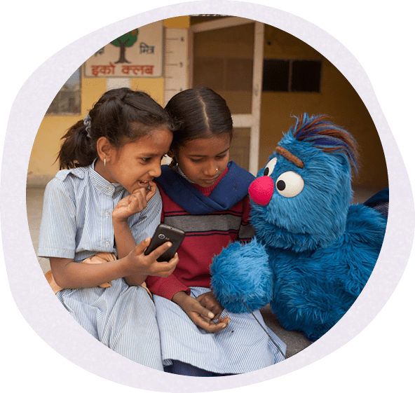 Two little girls sitting next to the cookie monster while holding a cell phone