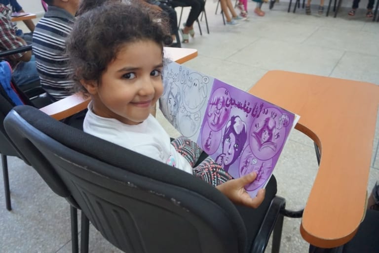 A girl reads a book in Arabic created by Asafeer through ACR GCD's No Lost Generation Tech Summit prize.