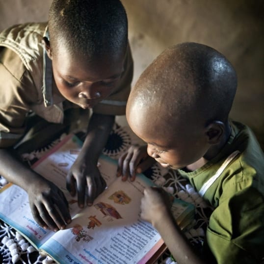 Two African children read a book together.