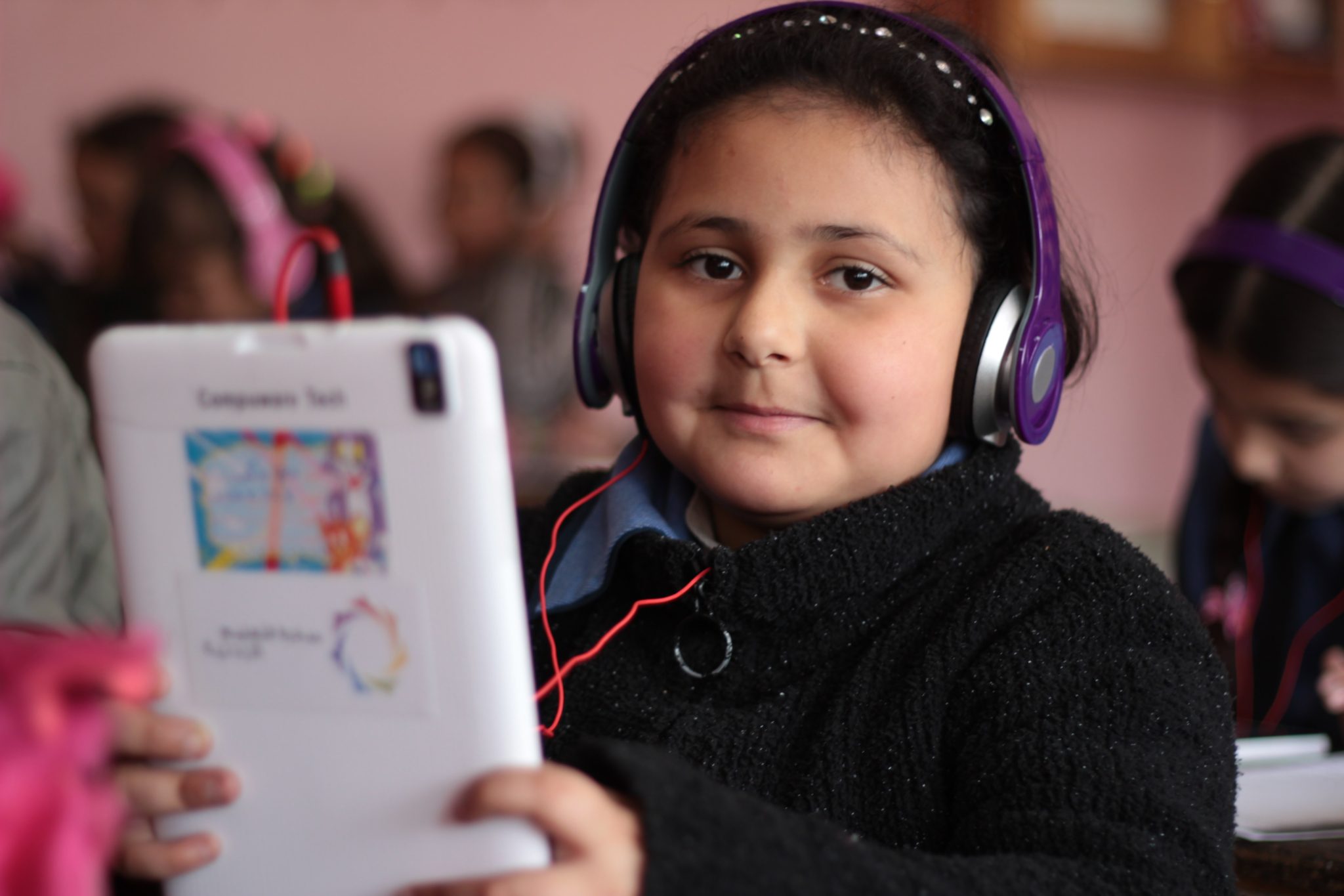 A girl with headphones and holding a table smiles at the camera